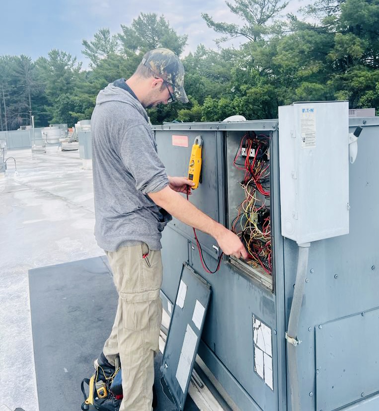 Technician using a clamp meter during a rooftop HVAC maintenance visit